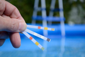 Hand with measuring strips to control water quality in swimming pools