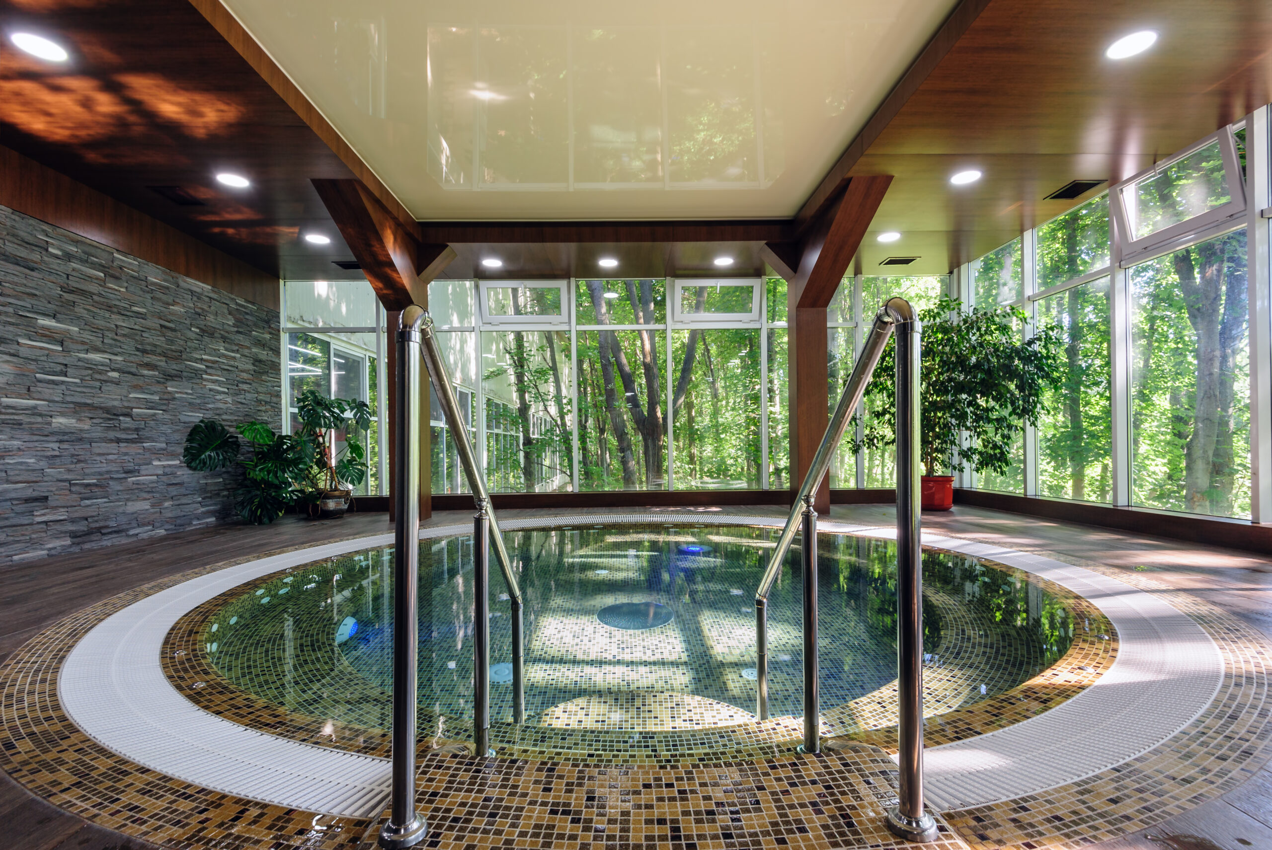 A round pool with a natural aesthetic, surrounded by lush greenery and offering a serene view of nature through glass walls or windows.