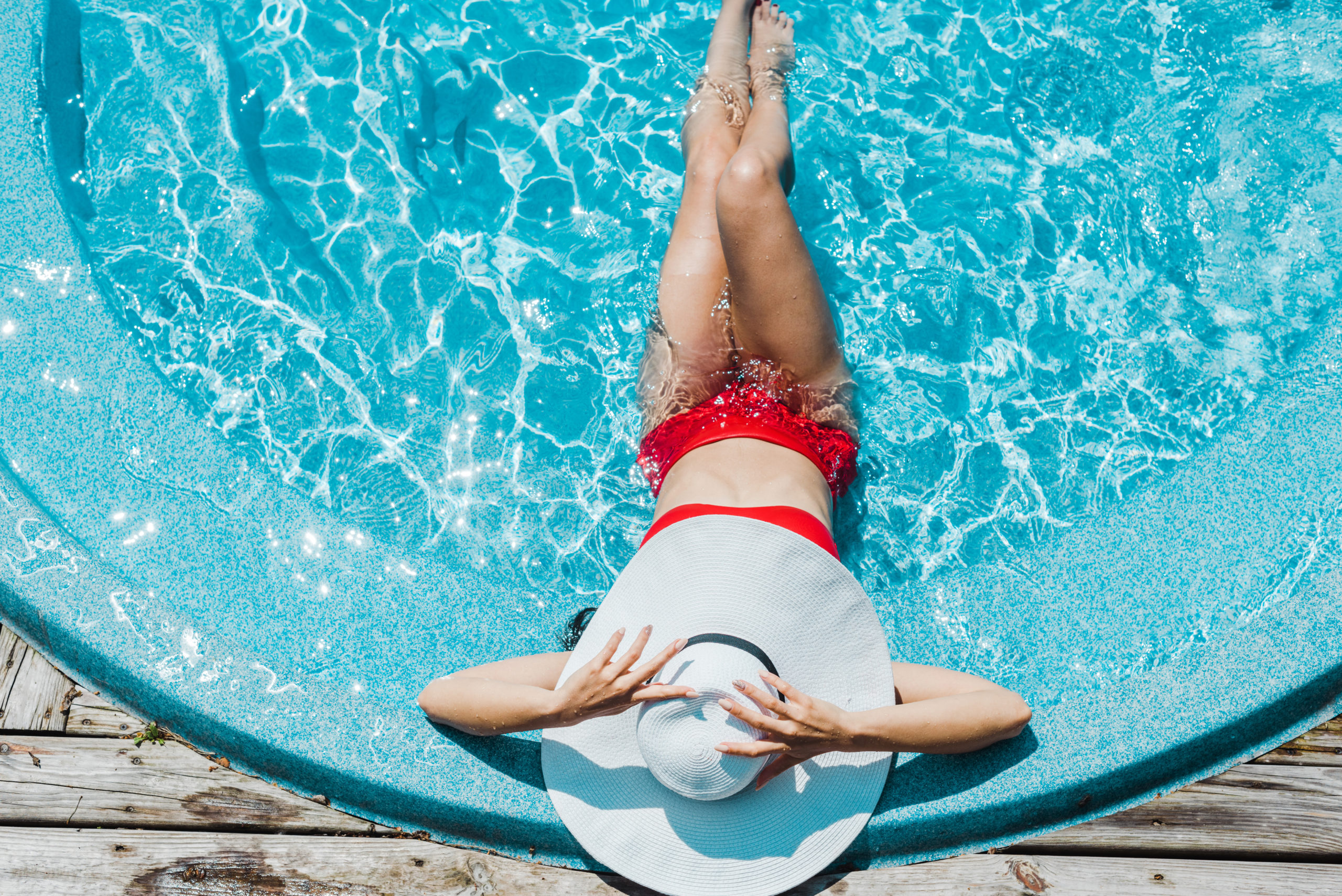 A woman wearing a hat, relaxing by the pool in direct sunlight