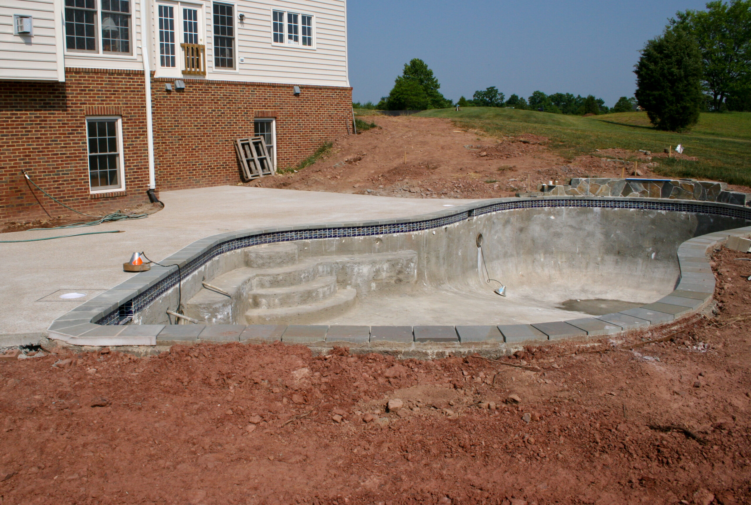 An empty pool that remains unfinished, with construction equipment and materials around it, awaiting completion.