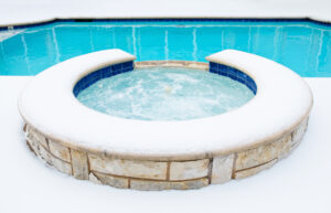 Outdoor residential hot tub or spa by swimming pool surrounded by snow in the winter