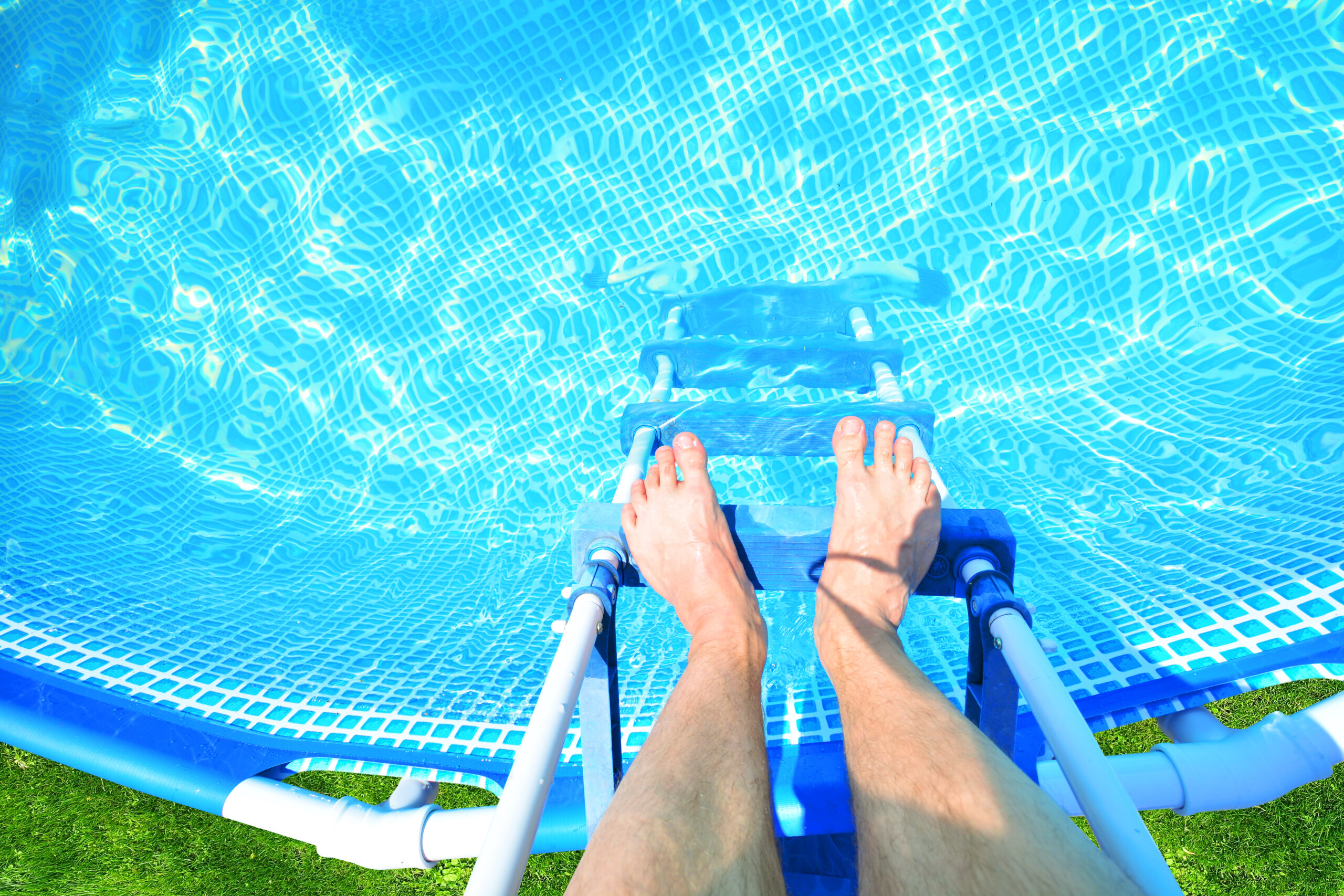 Feet resting on the ladder steps of a swimming pool, ready to climb in of the water for a refreshing swim