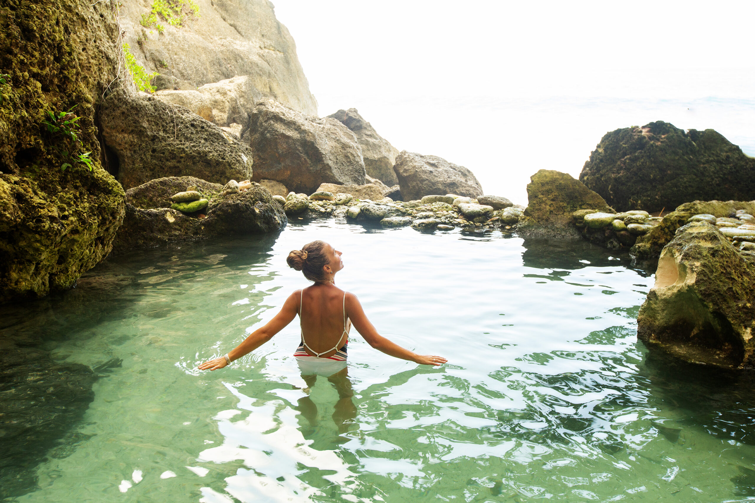 A woman joyfully enjoying an eco-friendly pool surrounded by natural rocks, immersing herself in a tranquil and environmentally conscious poolside experience