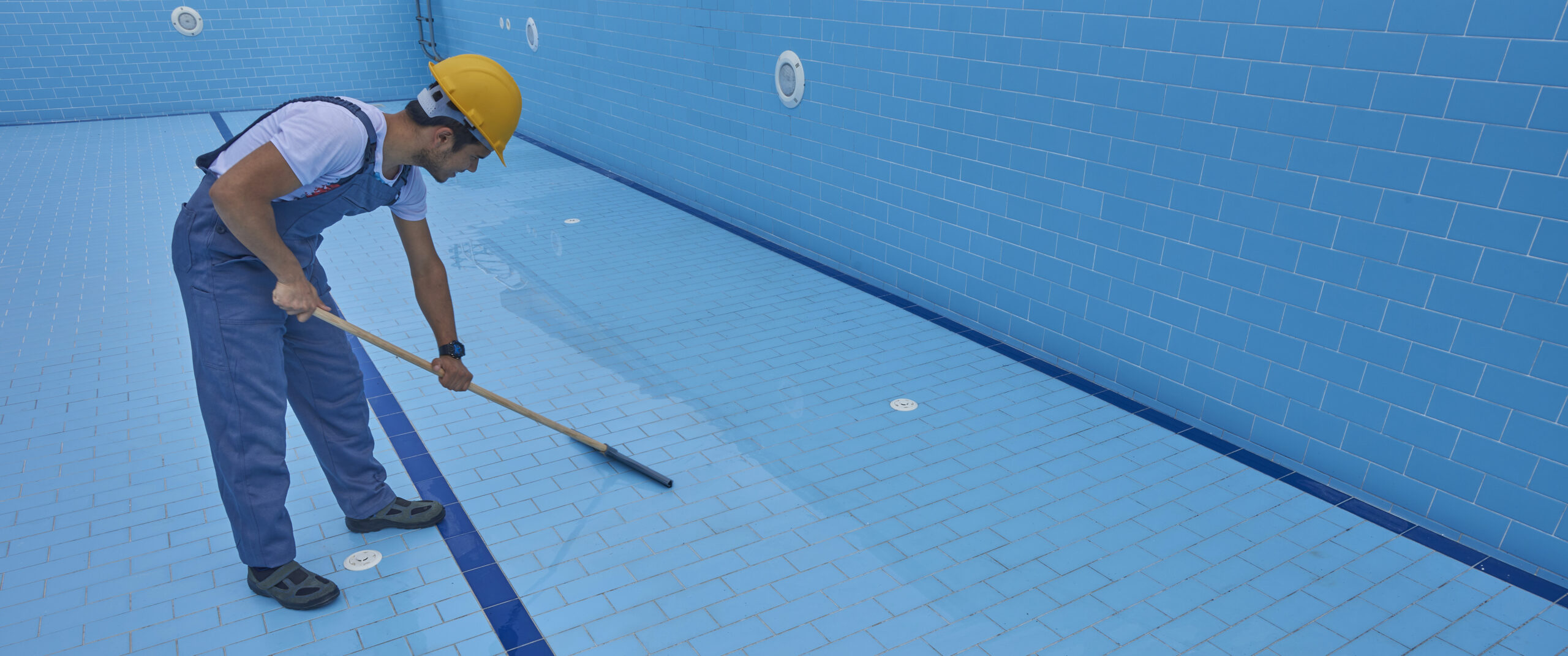 A man scrubbing tiles in a swimming pool, ensuring they remain clean and free of algae and debris.