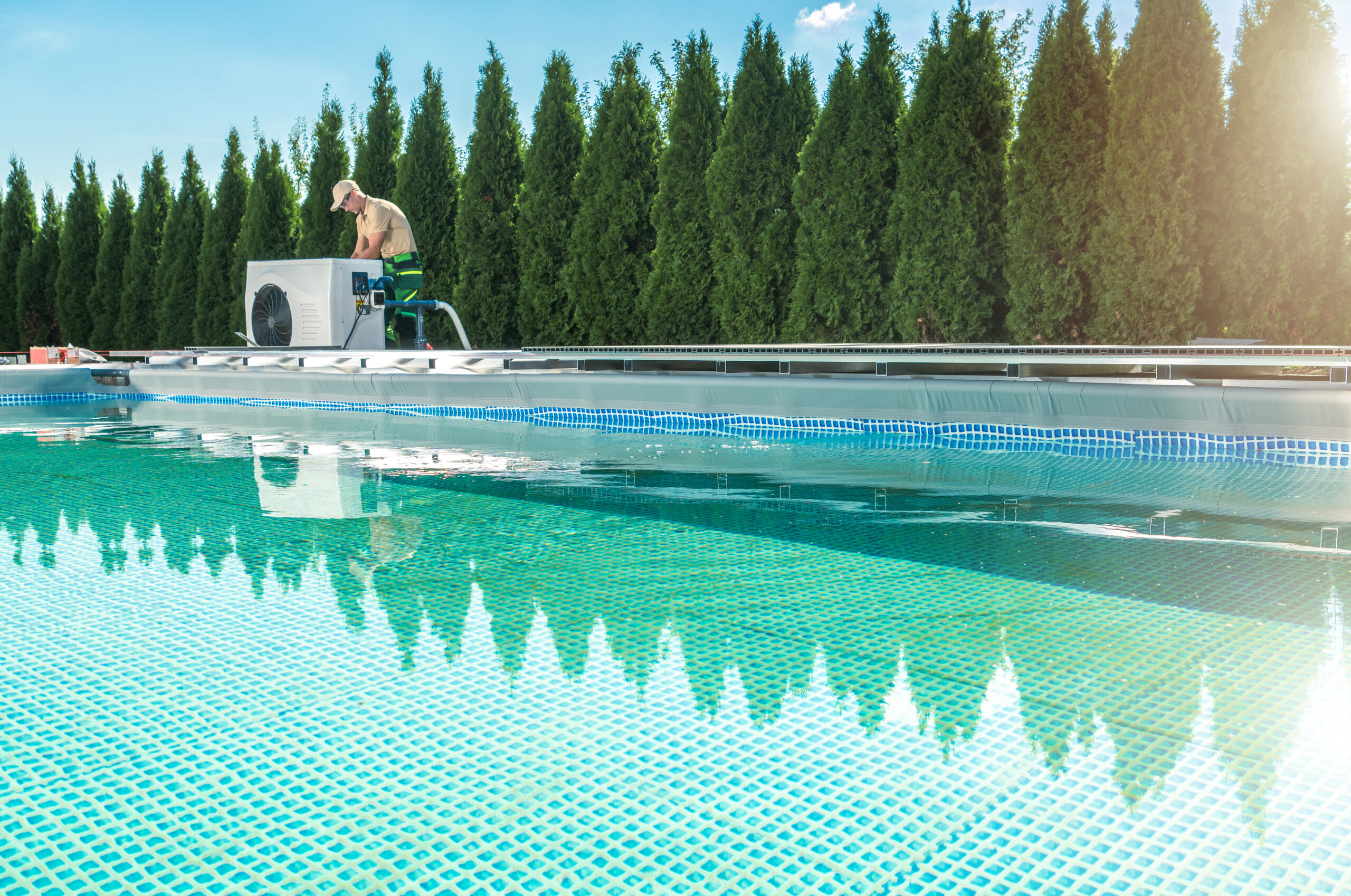 A man setting up a pool heater near a swimming pool, adjusting the equipment to regulate the water temperature for optimal comfort.