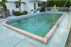 Dirty outdoor private pool with algae near the plants and trees outside the building at Miami, FL