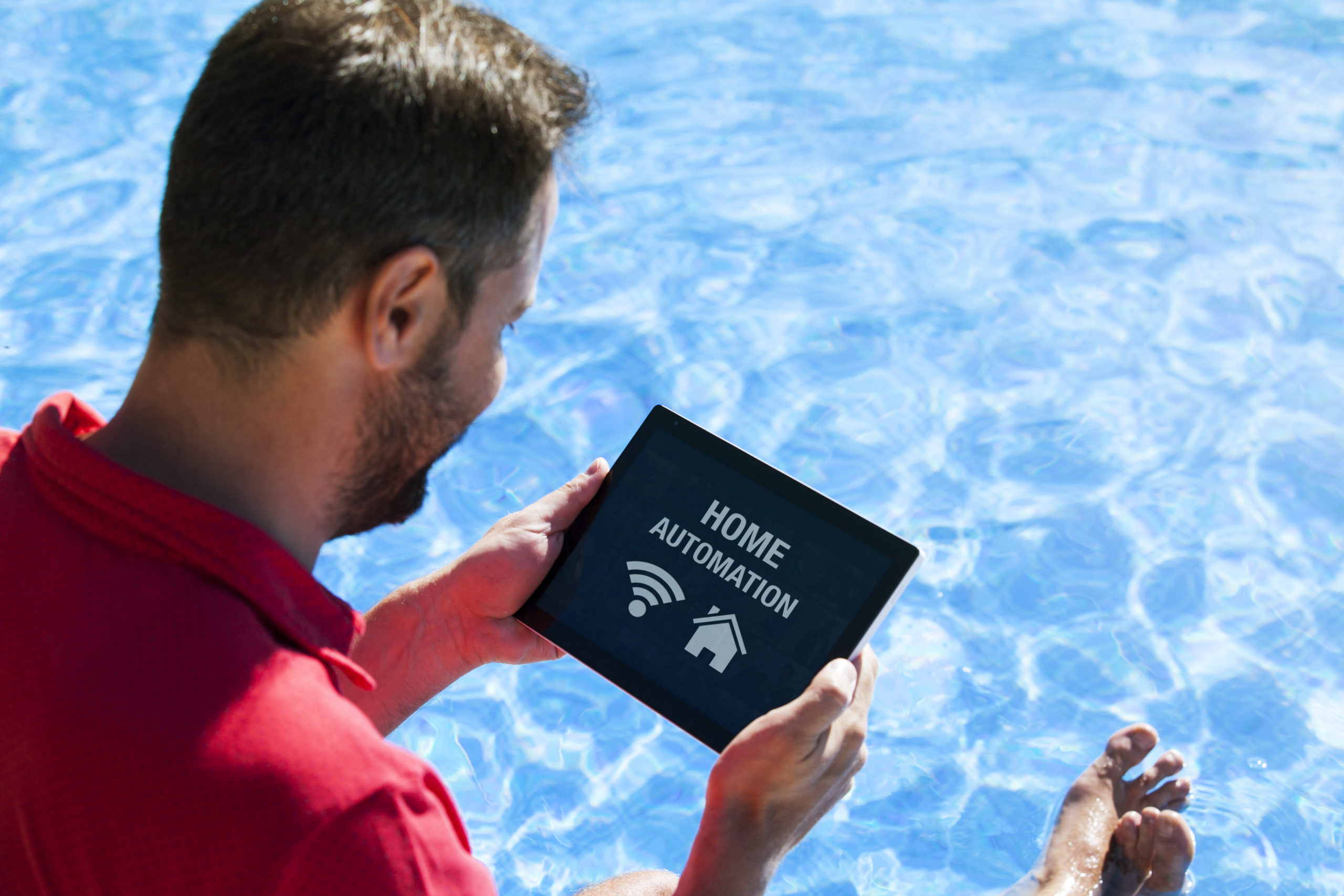 A man holding a pool automation gadget or control device, which allows for the remote management and automation of various pool functions and features.