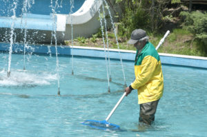 A man cleaning a swimming pool, using a brush and pool cleaning equipment