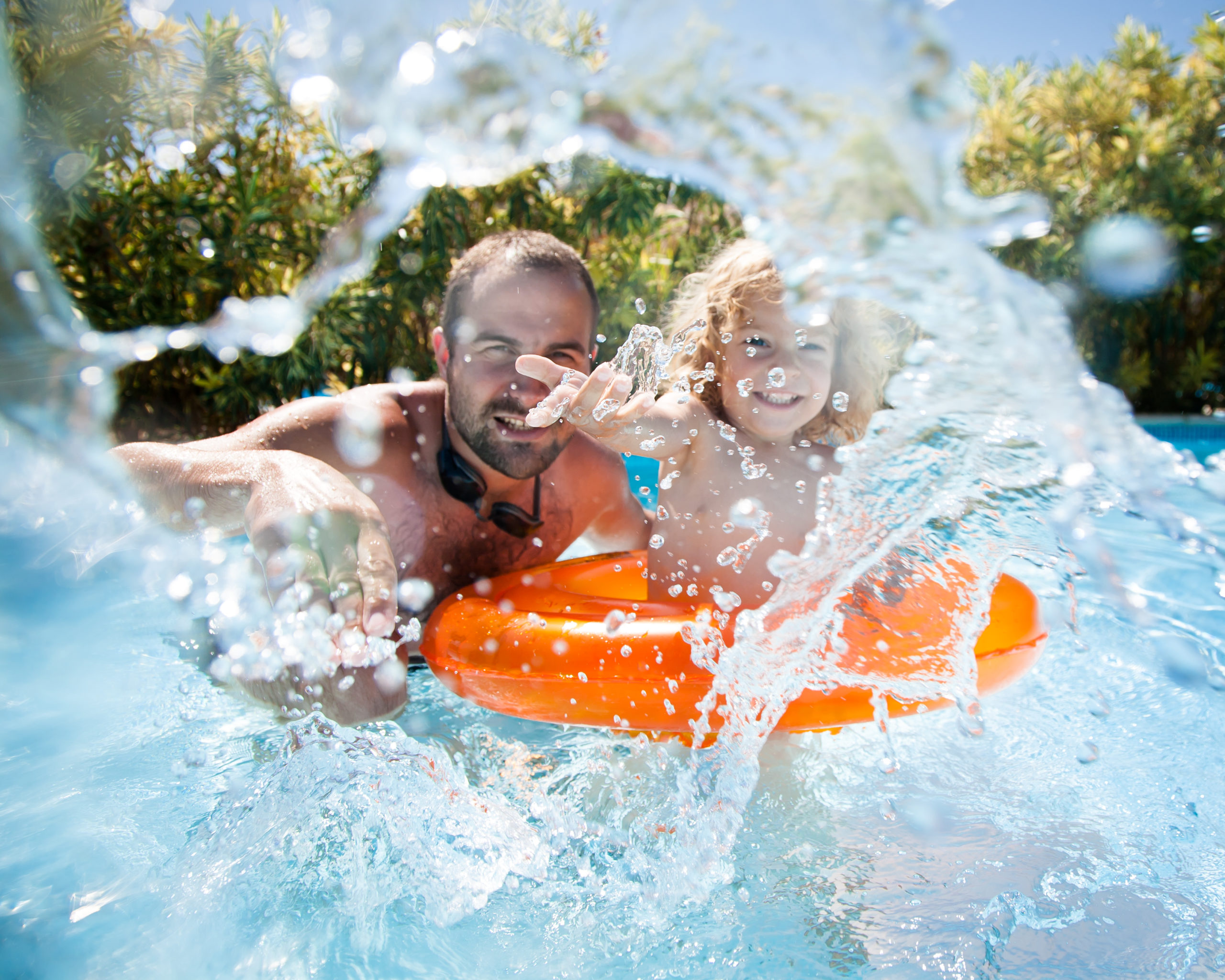 A man and his child joyfully splashing water in the pool