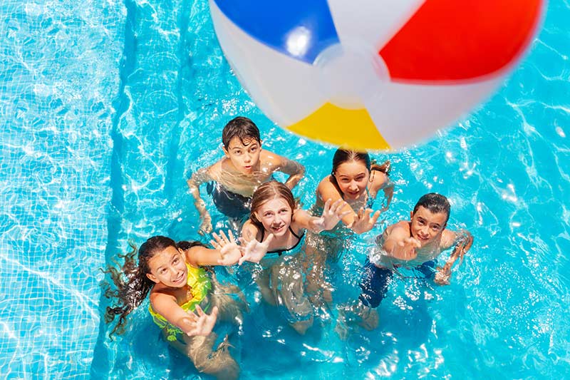 Children playing with a colorful ball at the pool, splashing water and enjoying a sunny day
